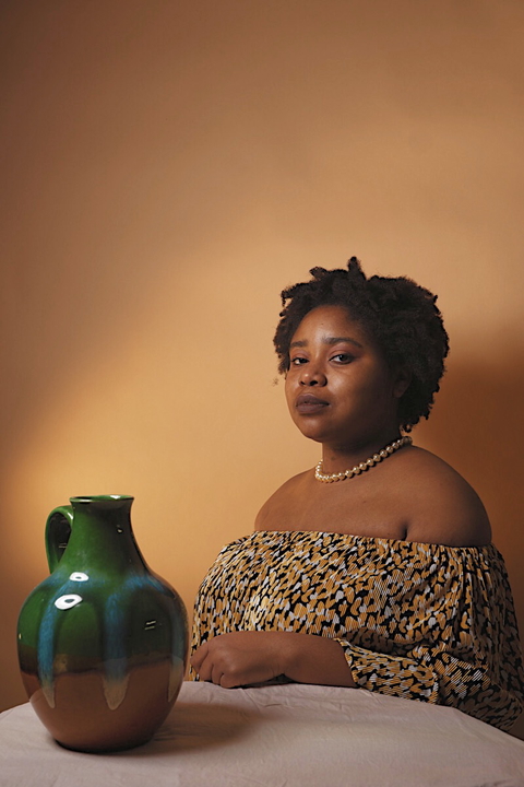 A woman poses with a ceramic vase in a warm-toned, softly lit studio portrait, perfect for art or lifestyle editorial.