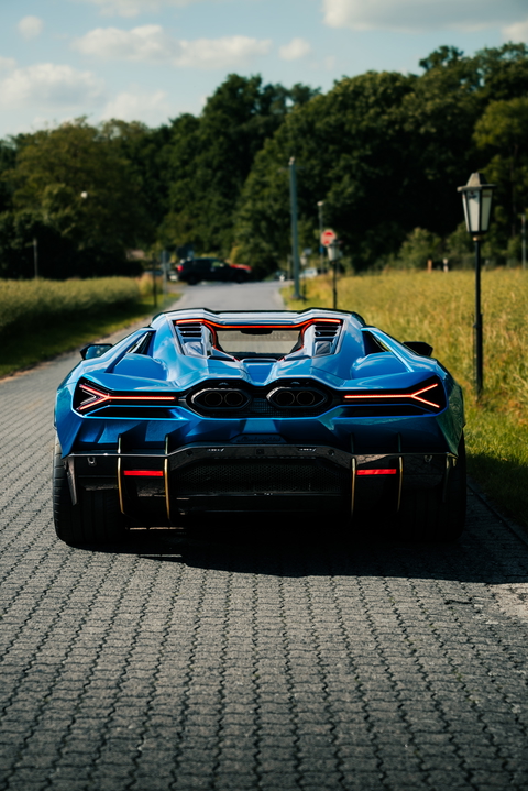 A vibrant blue sports car sits on a road surrounded by trees, showcasing its sleek design.