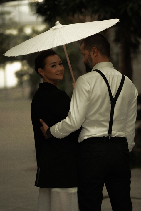 A stylish couple shares a tender moment beneath a white umbrella, exuding timeless elegance.