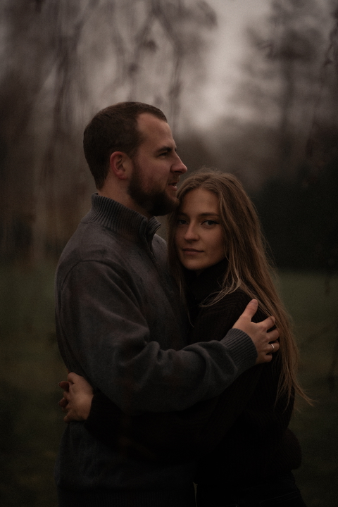 A loving couple embraces outdoors in a soft, natural setting, exuding warmth and affection.