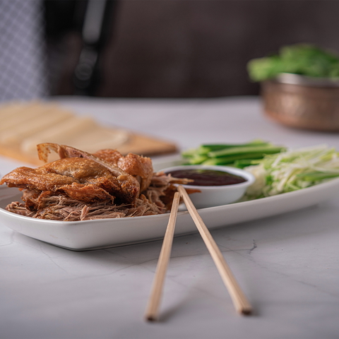 Close-up of Peking duck, pancakes, cucumber, spring onions and hoisin sauce on a white serving platter.
