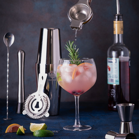 A refreshing cocktail is being prepared and garnished with rosemary and citrus, set against a stylish bar setting.