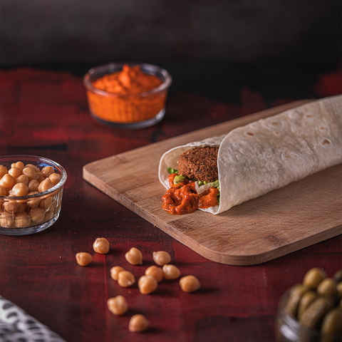 A falafel wrap with chickpeas and dip on a wooden board, perfect for food blogs or social media.