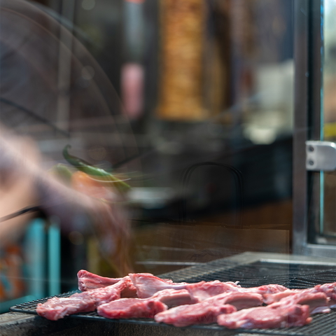 Raw meat is being grilled on a charcoal grill inside a restaurant for food promotion.