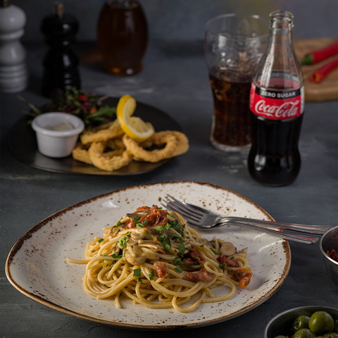 A plate of spaghetti, squid rings, and coca-cola on a table in a restaurant setting.