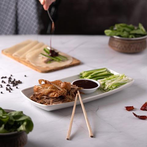 Peking duck served with pancakes, cucumber, and sauce on a white marble table.