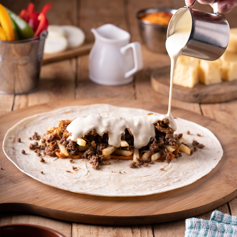 A close-up shot of a tortilla being prepared with meat, fries, and sauce on a wooden surface.