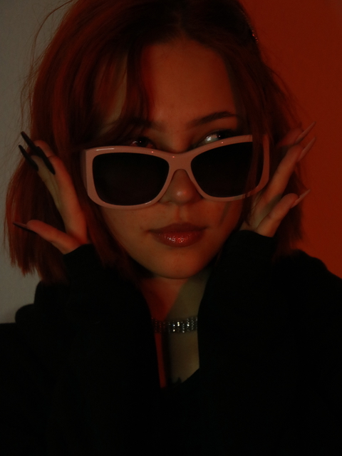 A woman with sunglasses and long nails poses in an editorial style portrait.