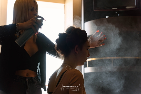 A woman is getting her hair styled with hairspray by a stylist in a salon.