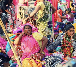A vibrant street market scene in India features women selling colorful textiles and saris in a bustling outdoor setting.