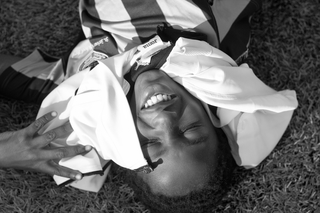 A smiling man lying on the grass in black and white, wearing a sports jersey.