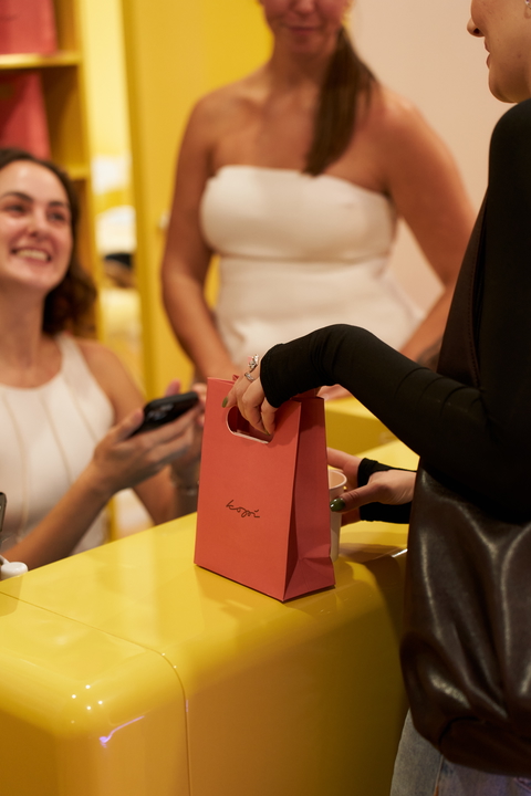 A customer receives a branded shopping bag at a modern retail counter in a cheerful, vibrant store.