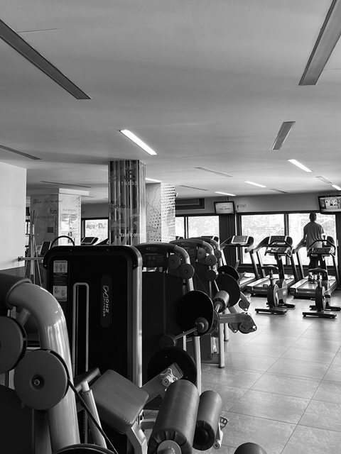 A monochrome shot inside a gym with equipment and a person using a treadmill.