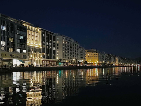 A scenic night view of a city's waterfront with illuminated buildings reflected in the water.