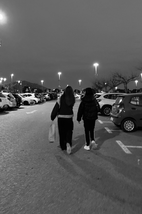 Two women walk through a parking lot at night in a monochrome image.