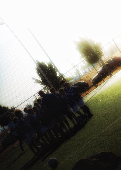 A soccer team is huddled together on a field, with a coach leading them in a motivational team talk.