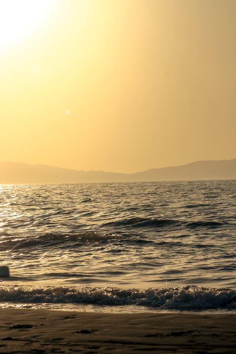 Golden sunlight over the sea with gentle waves and sandy beach, creating a tranquil seascape.