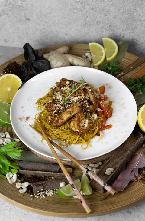 A delicious plate of chicken chow mein with chopsticks and citrus on a wooden tray, for a appetizing and shareable image.