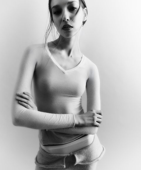 A young woman in a long-sleeved top poses in a black and white studio shot.