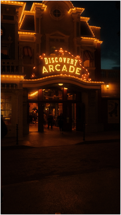 The brightly lit Discovery Arcade entrance invites visitors on a vibrant city street at night.
